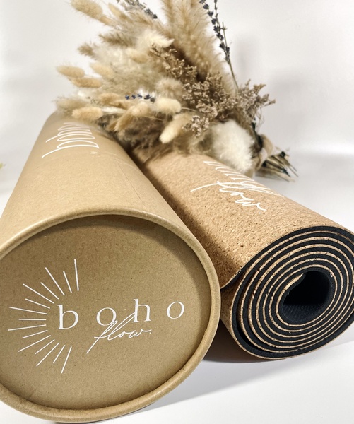 This static creative showcases a rolled yoga mat alongside a dried floral arrangement in a clean, high-key studio setting to evoke a sense of calm and natural wellness.